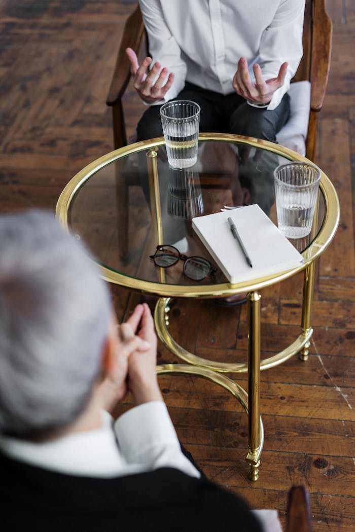about-01 Two adults discussing mental health in a counseling session across a glass table indoors.