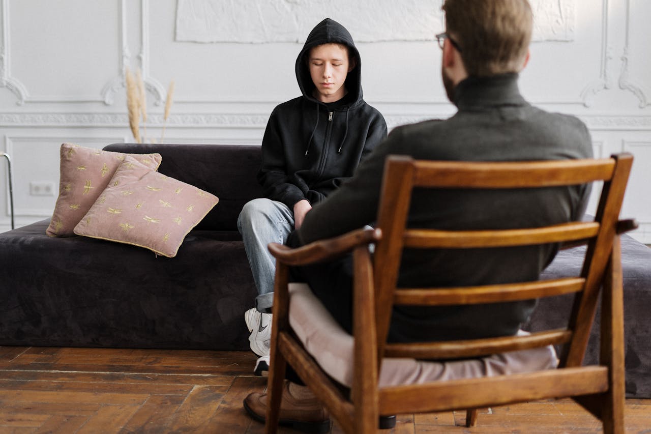 gallery-6 A teenager in hooded sweatshirt talks with a therapist in a modern, minimalistic studio.