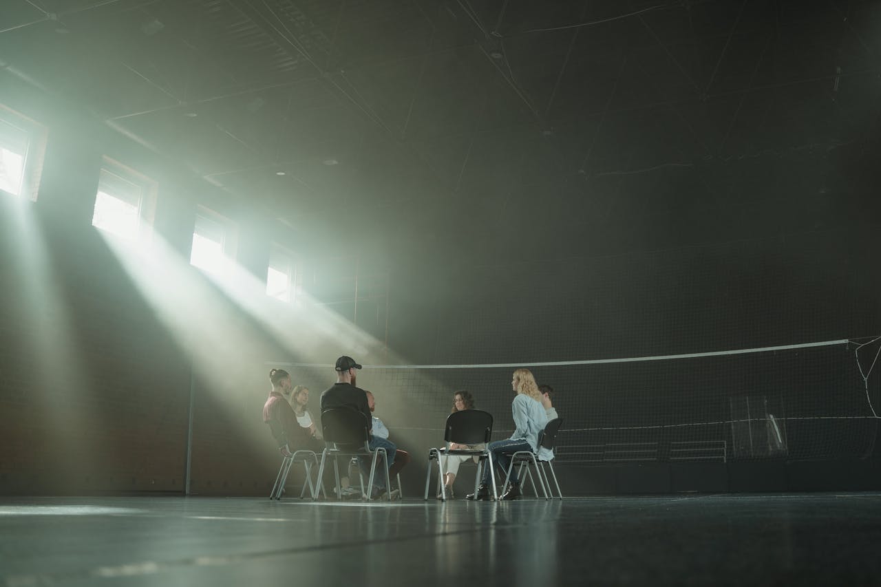 gallery-2 A small group of people participating in a support session, illuminated by sunrays in a spacious hall.
