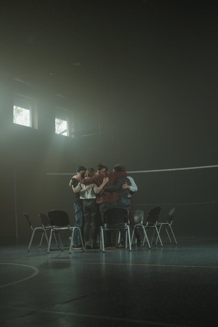 gallery-3 A diverse support group hugs in a dimly lit room, fostering unity and emotional support.