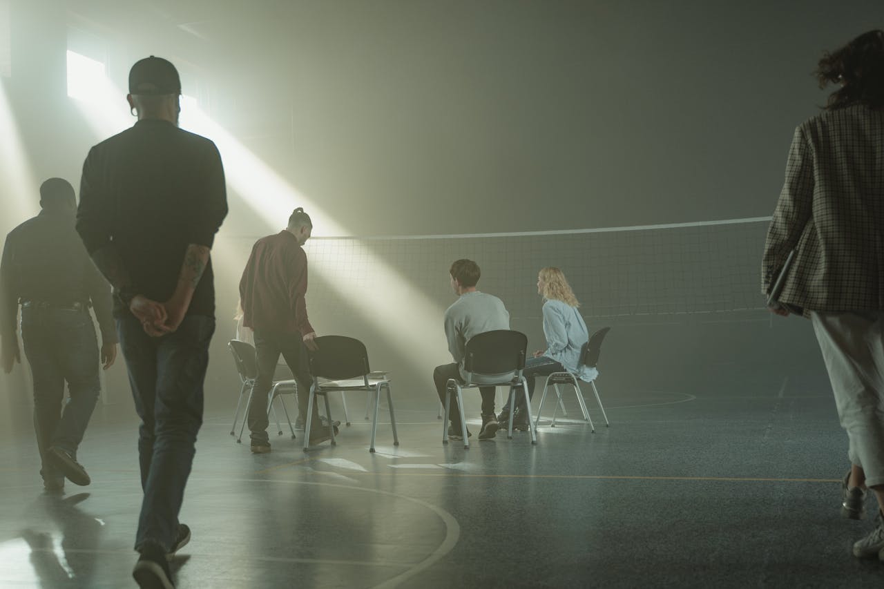 A group therapy session with diverse adults in a dimly lit gymnasium, highlighting mental health support.
