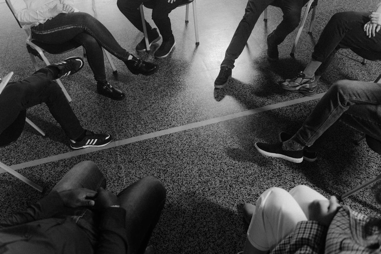 our-services-1 Black and white photo of a support group session indoors with diverse participants.