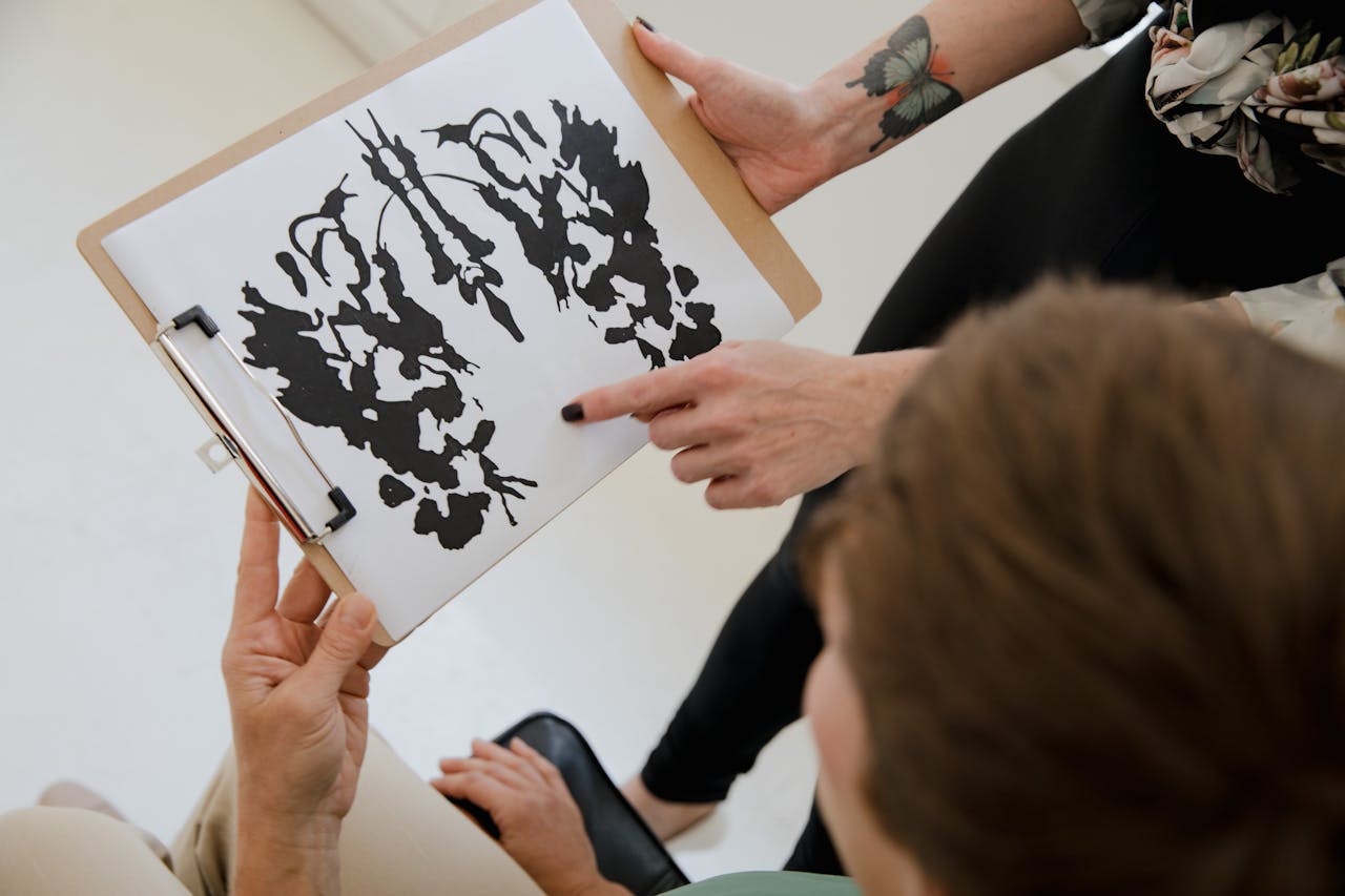 gallery-4 Hands holding a clipboard with an inkblot for psychological analysis.